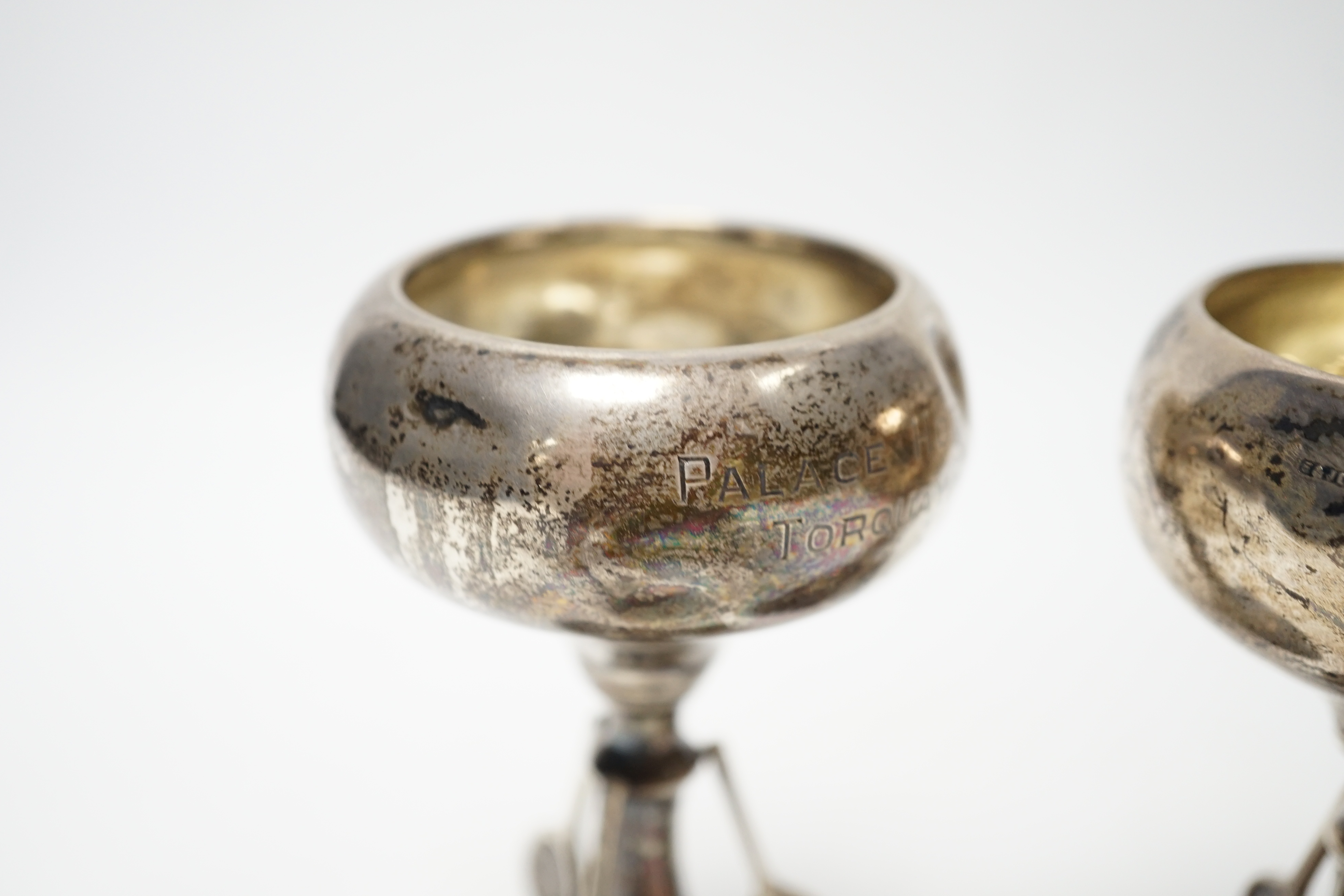 A set of three small George V silver tennis related trophy cups, with racket supports and engraved inscriptions, E & J Leek, 92mm, two with plinth bases.